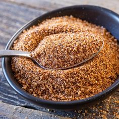 a spoon full of ground cinnamon sits in a black bowl on a wooden table top