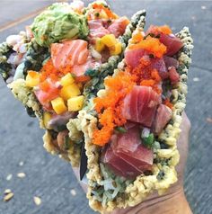 a person holding food in their hand on the street with lots of different toppings