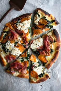 a pizza with cheese, ham and spinach on it next to a spatula