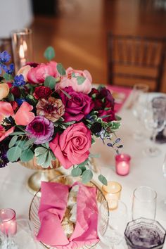 a vase filled with pink and purple flowers on top of a white table covered in candles