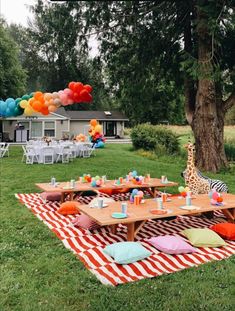 an outdoor party with giraffes and balloons on the grass in front of a tree