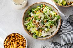 two bowls filled with lettuce and chickpeas next to a glass of milk