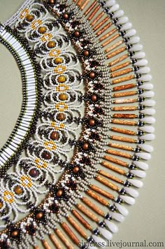 an intricate beaded necklace with gold and white beads on it's sides, in the shape of a half circle