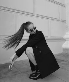 a woman sitting on the ground with her hair blowing in the wind and wearing sunglasses