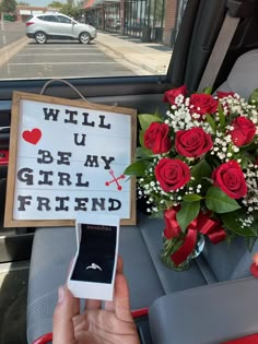 a person holding a cell phone next to a bouquet of roses and a sign that says will u be my girlfriend