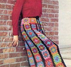 a woman leaning against a brick wall wearing a crocheted skirt and red sweater