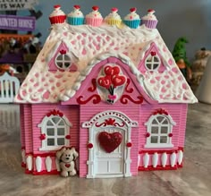 a pink doll house with cupcakes on the roof and a teddy bear next to it