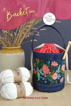 two balls of yarn are sitting next to a basket with knitting needles and crochet hooks