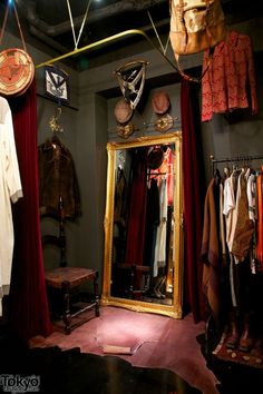 a room filled with lots of clothes hanging on hooks next to a large gold framed mirror