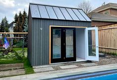 a small pool house next to a backyard with a swimming pool and wooden fenced in area