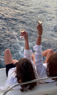 two women are sitting on a boat holding wine glasses in their hands as they look out at the water