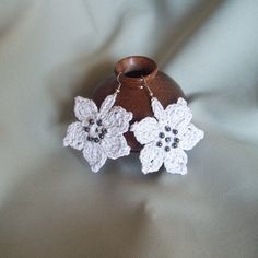 two crocheted flowers are attached to a brown vase on a white fabric background