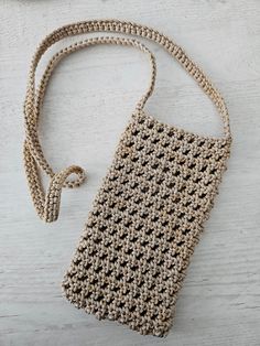 a crocheted purse sitting on top of a white wooden table next to a cell phone