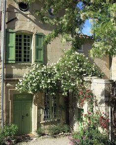 an old stone house with green shutters and flowers