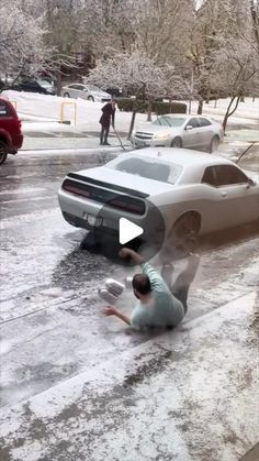 a man kneeling down next to a parked car in the street with snow on it