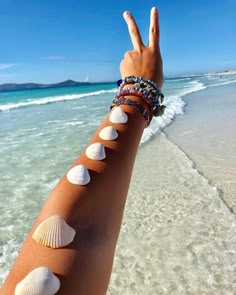 a woman's arm with seashells and bracelets on it at the beach