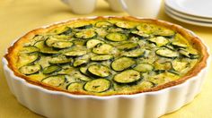 a quiche with zucchini and cheese in a white dish on a yellow tablecloth