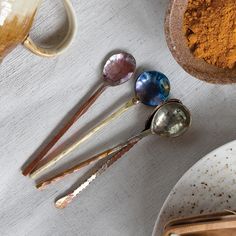 three spoons are sitting on a table next to some spices and other utensils