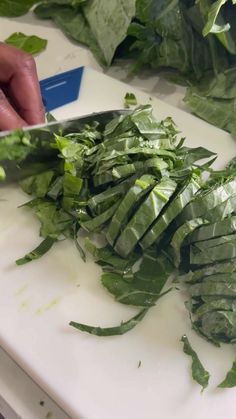 someone cutting up some greens on a white counter