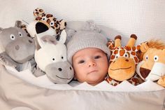 a baby laying in bed with stuffed animals on it's back and wearing a hat