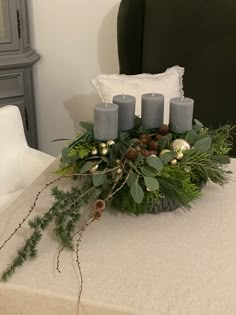 a table topped with candles and greenery on top of a white cloth covered table