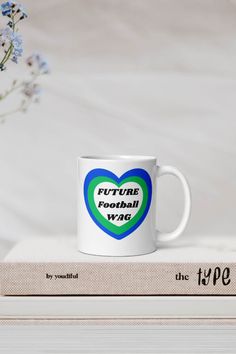 a blue and green heart shaped coffee mug sitting on top of a stack of books