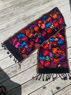 two scarfs with flowers on them sitting on a wooden floor next to someone's feet