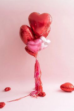 two red heart shaped balloons tied to a string on a pink background with confetti