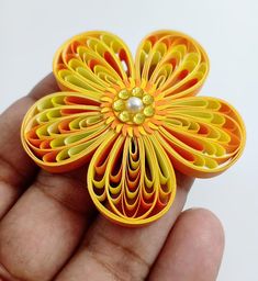 a hand holding a yellow and orange flower brooch