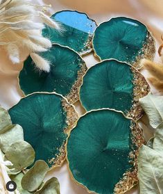 four green leaf shaped plates sitting on top of a white cloth covered table next to feathers