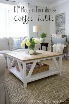 a coffee table with flowers on top in a living room area that has white furniture and blue pillows