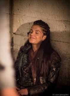 a woman with long hair wearing a leather jacket and smiling at someone in the background