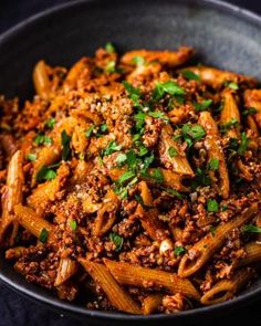 pasta with meat and parsley in a black bowl on a blue tablecloth, top view