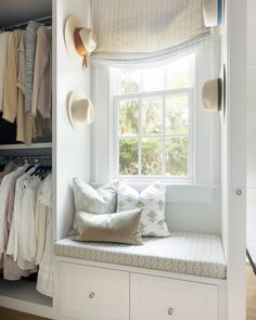 a window seat in the corner of a closet with pillows and hats hanging on it