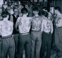 a group of men standing next to each other in front of a bar with tattoos on their back