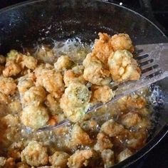 fried food being cooked in a skillet with tongs