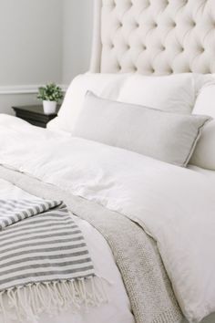 a bed with white linens and pillows on it's headboard in a bedroom