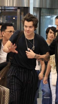 a man in black shirt and striped pants walking through an airport with other people behind him