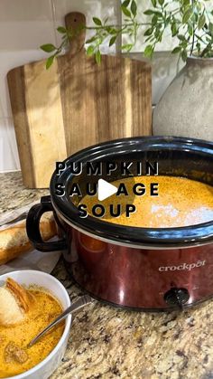 a slow cooker with pumpkin soup in it and a bowl of bread next to it