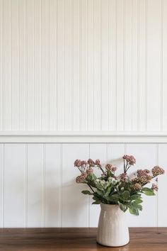 a vase filled with flowers sitting on top of a wooden table next to a wall