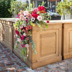 a flower arrangement is placed on the back of a wooden church pew with red and pink flowers