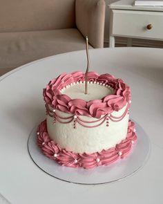 a white cake with pink icing and a single candle sticking out of the top