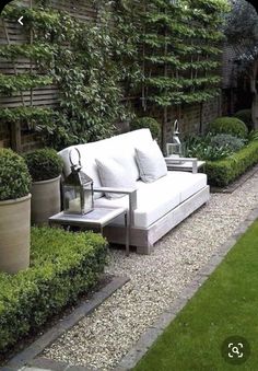 a white couch sitting in the middle of a lush green yard with potted plants