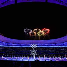 the olympic logo is lit up at night in front of an arena with people watching