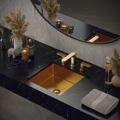 a bathroom sink with gold faucet and black counter top next to mirror above it