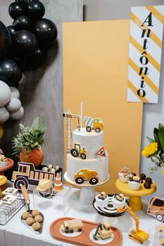 a table topped with lots of cakes and desserts next to balloons in the shape of trucks