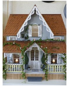 a doll house is decorated with flowers and greenery on the front porch, along with potted plants