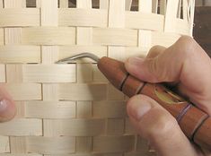 two hands are working on a woven basket