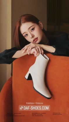 a woman leaning on an orange chair with her hand on the top of one shoe