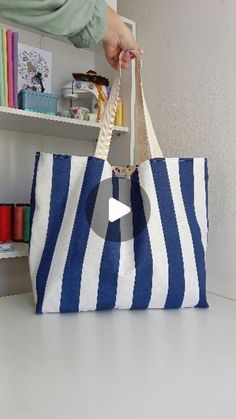 a person is holding a blue and white striped tote bag in front of a bookshelf